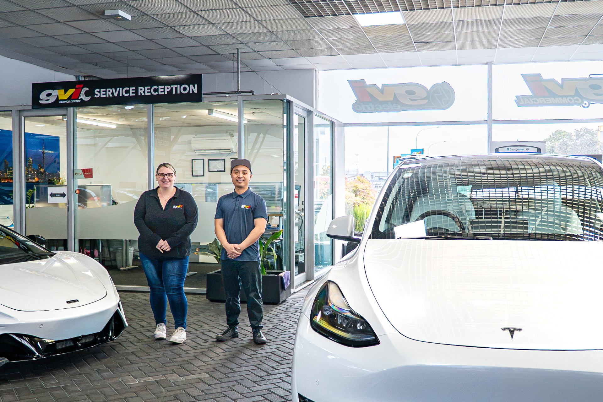 GVI Service Centre reception in Penrose, with two staff members between a Tesla and a McLaren